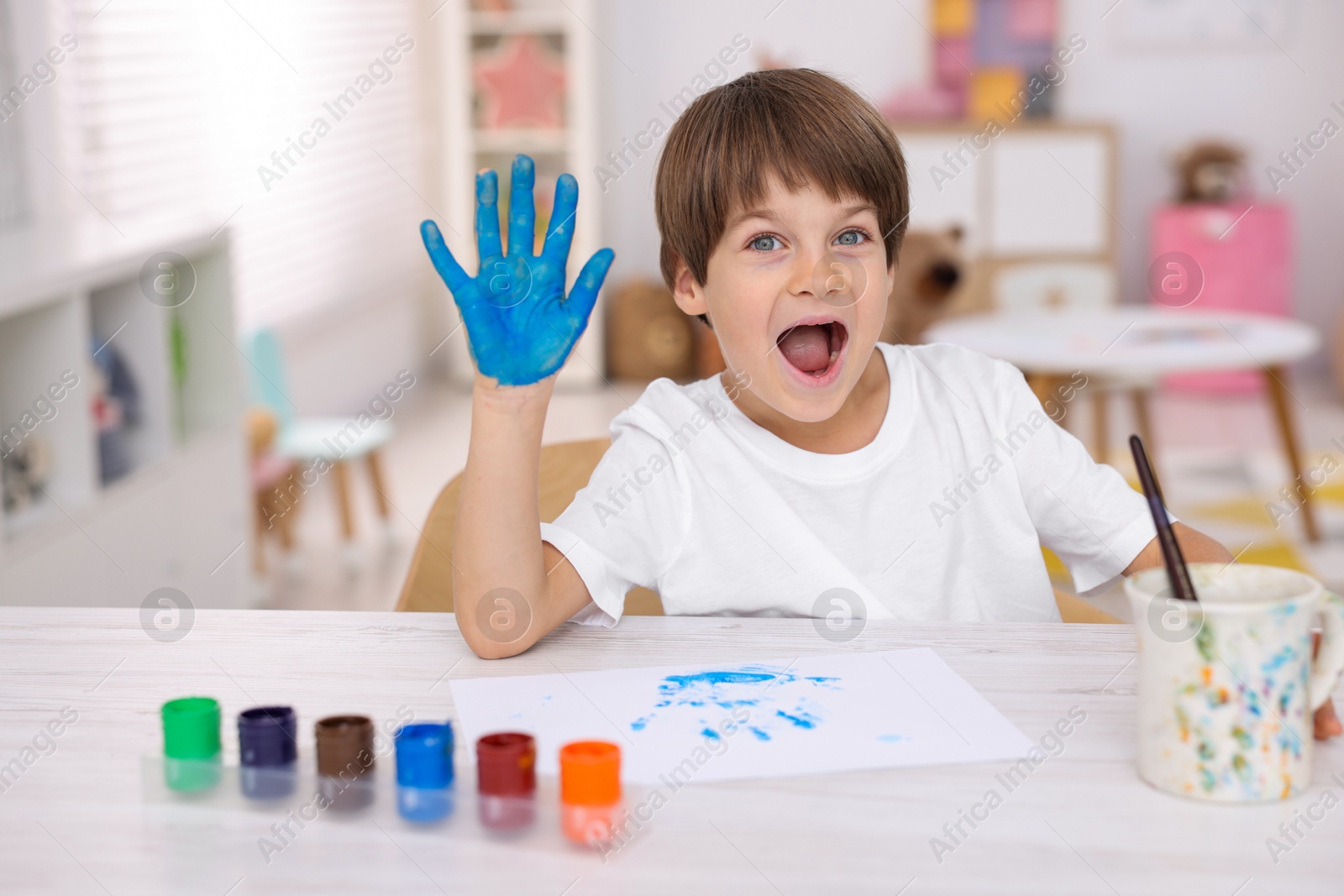 Photo of Happy boy drawing with palm at light wooden table in kindergarten