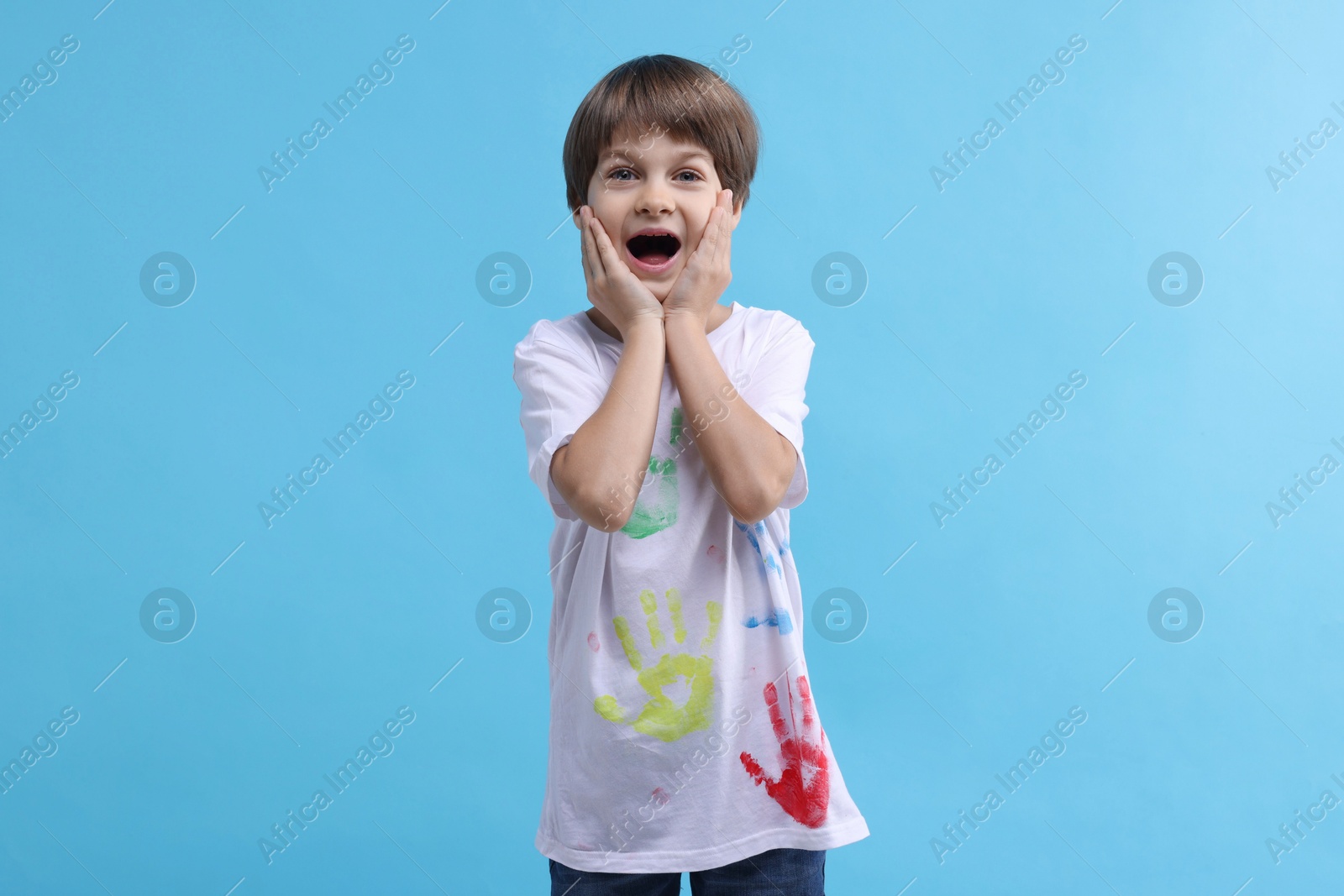 Photo of Portrait of emotional boy in t-shirt with handprints drawings on light blue background