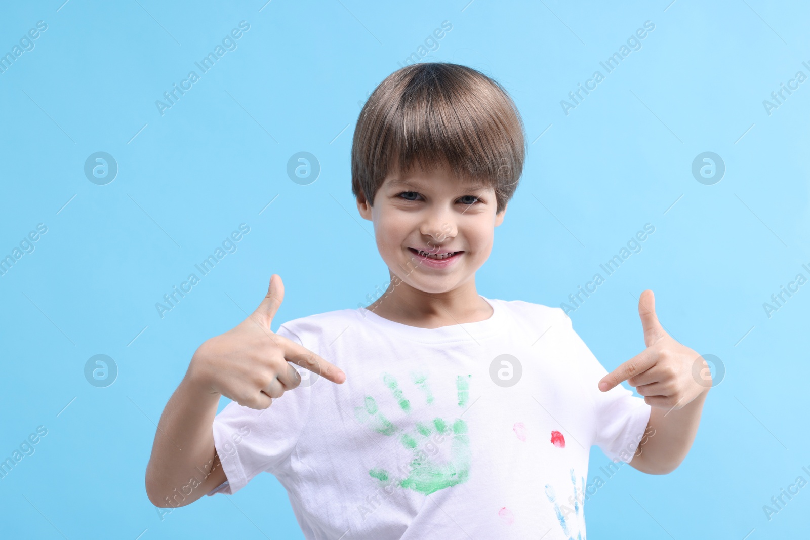 Photo of Portrait of happy boy pointing at his t-shirt with handprints drawings on light blue background