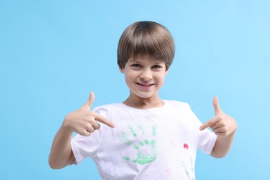 Photo of Portrait of happy boy pointing at his t-shirt with handprints drawings on light blue background