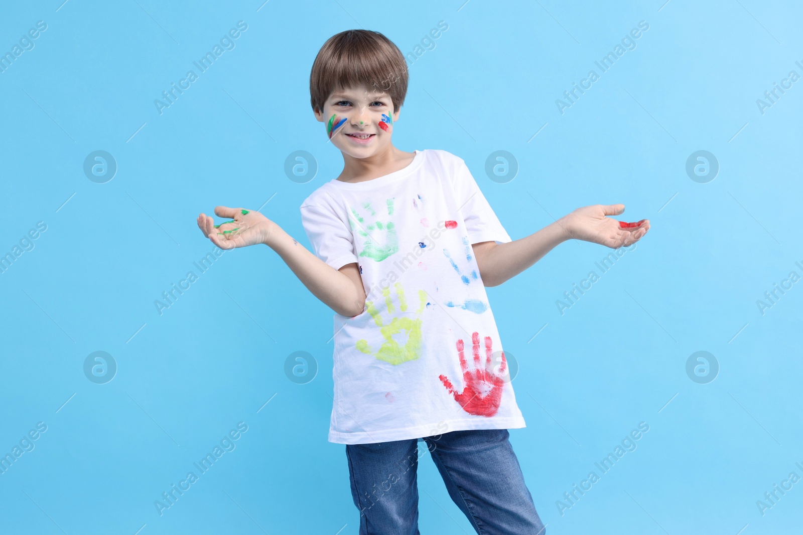 Photo of Portrait of smiling boy smeared in paint on light blue background