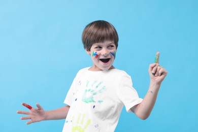 Photo of Happy boy smeared in paint had idea for his drawing on light blue background