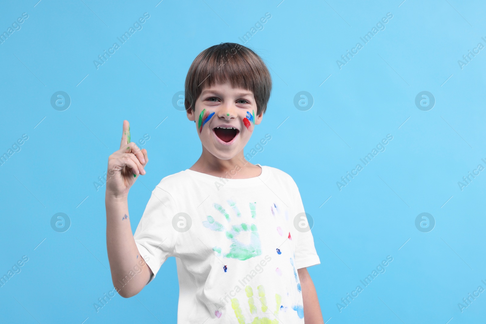 Photo of Cute boy smeared in paint had idea for his drawing on light blue background