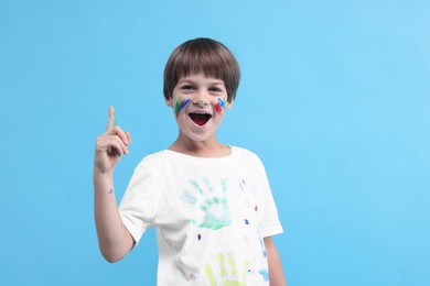 Photo of Cute boy smeared in paint had idea for his drawing on light blue background