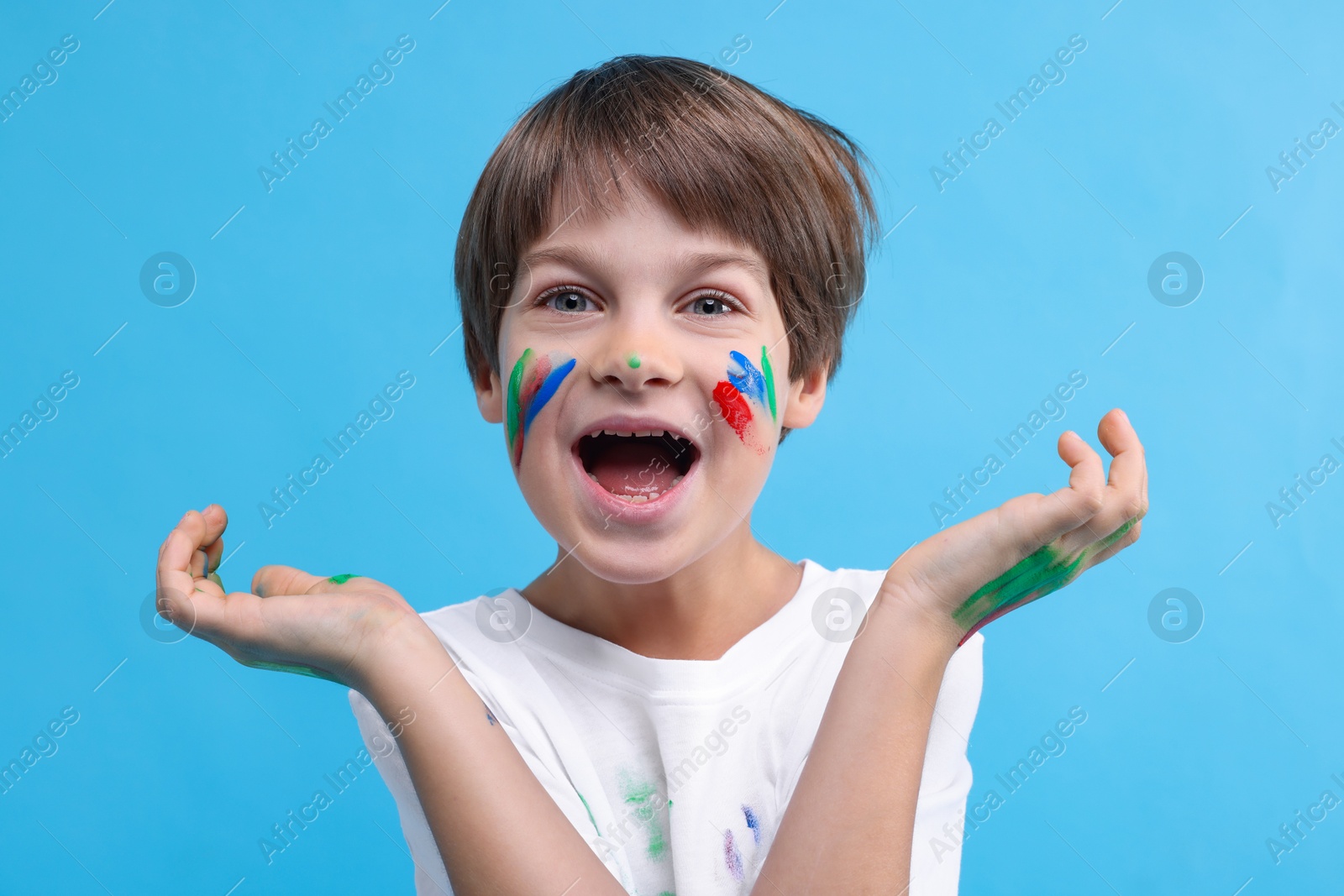 Photo of Portrait of funny boy smeared in paint on light blue background