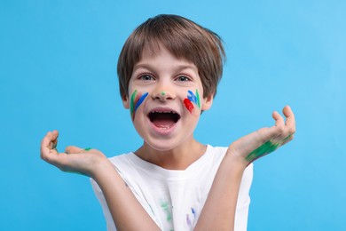 Photo of Portrait of funny boy smeared in paint on light blue background