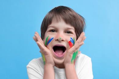 Photo of Portrait of funny boy smeared in paint on light blue background