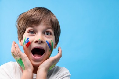 Photo of Portrait of funny boy smeared in paint on light blue background. Space for text