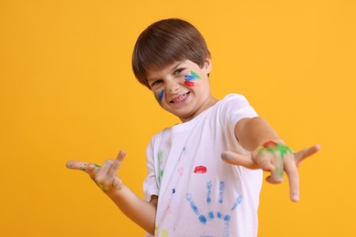 Photo of Portrait of happy boy smeared in paint on orange background