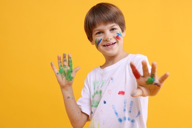 Photo of Portrait of happy boy smeared in paint on orange background. Space for text