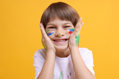 Photo of Portrait of happy boy smeared in paint on orange background