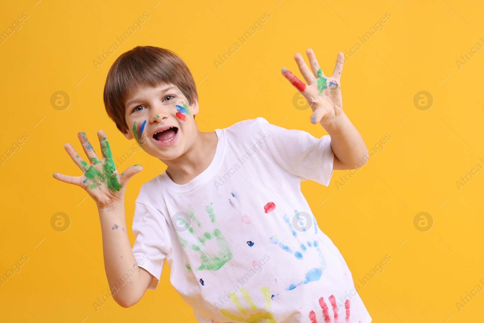 Photo of Portrait of funny boy smeared in paint on orange background