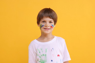 Photo of Portrait of happy boy smeared in paint on orange background