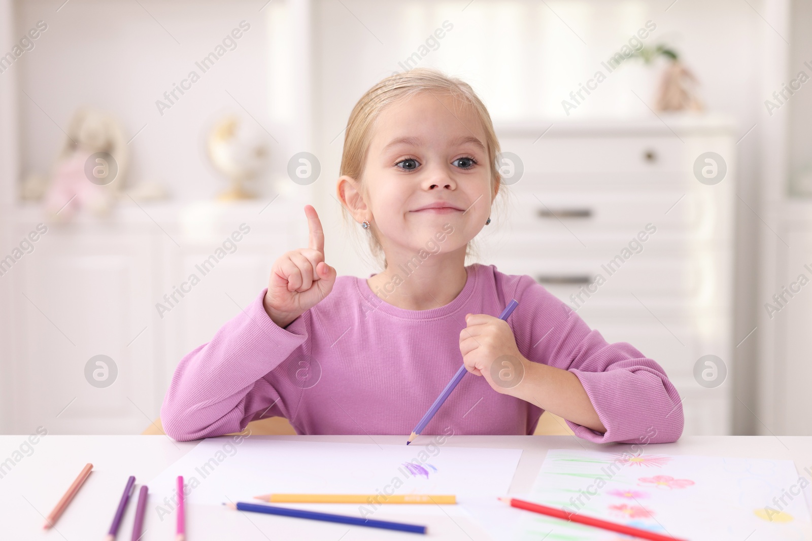 Photo of Cute girl had idea for her drawing at white table in kindergarten