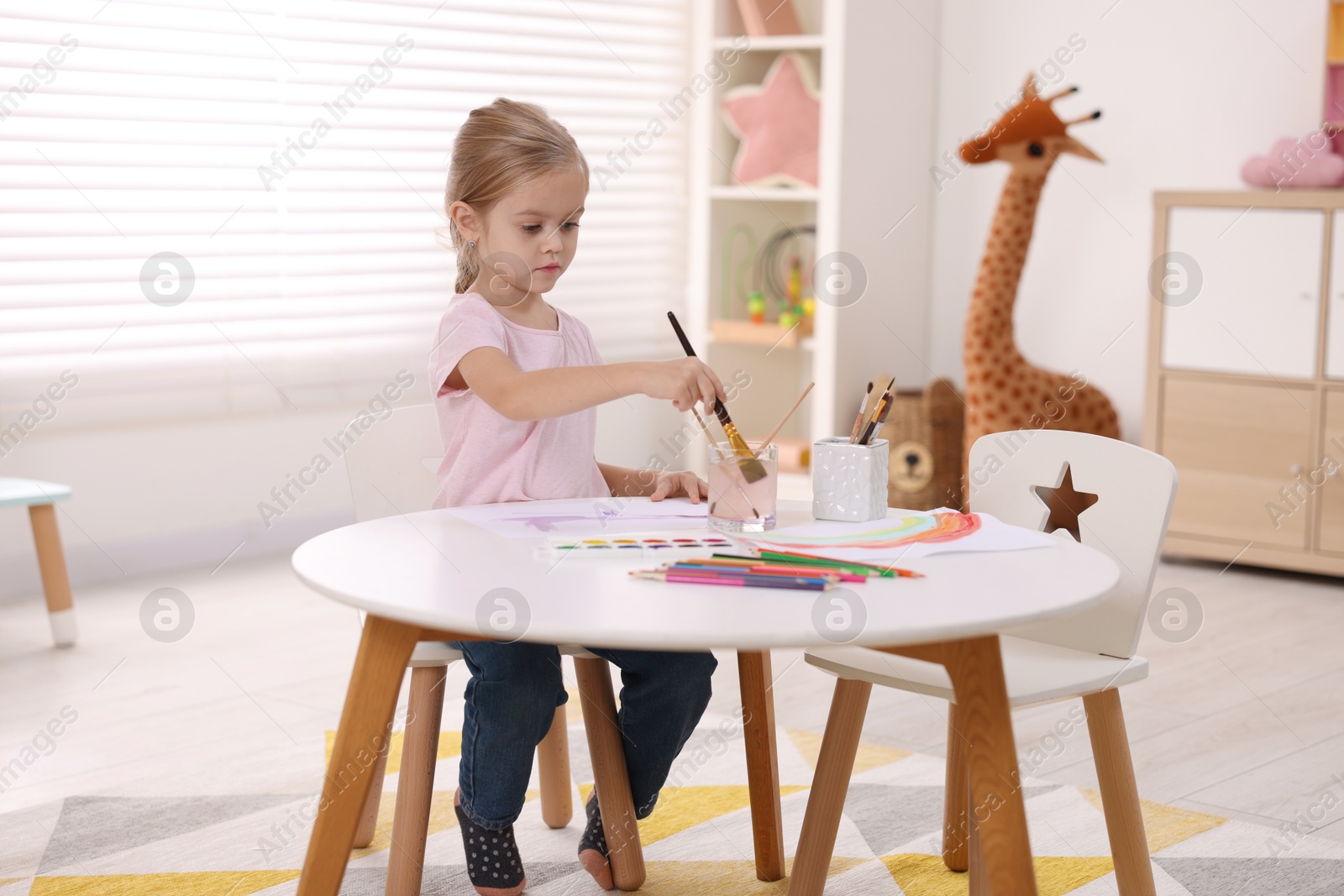 Photo of Cute girl drawing at white table in kindergarten