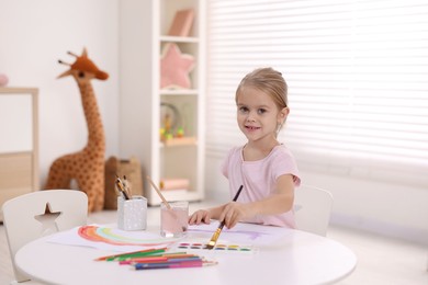 Photo of Smiling girl drawing at white table in kindergarten