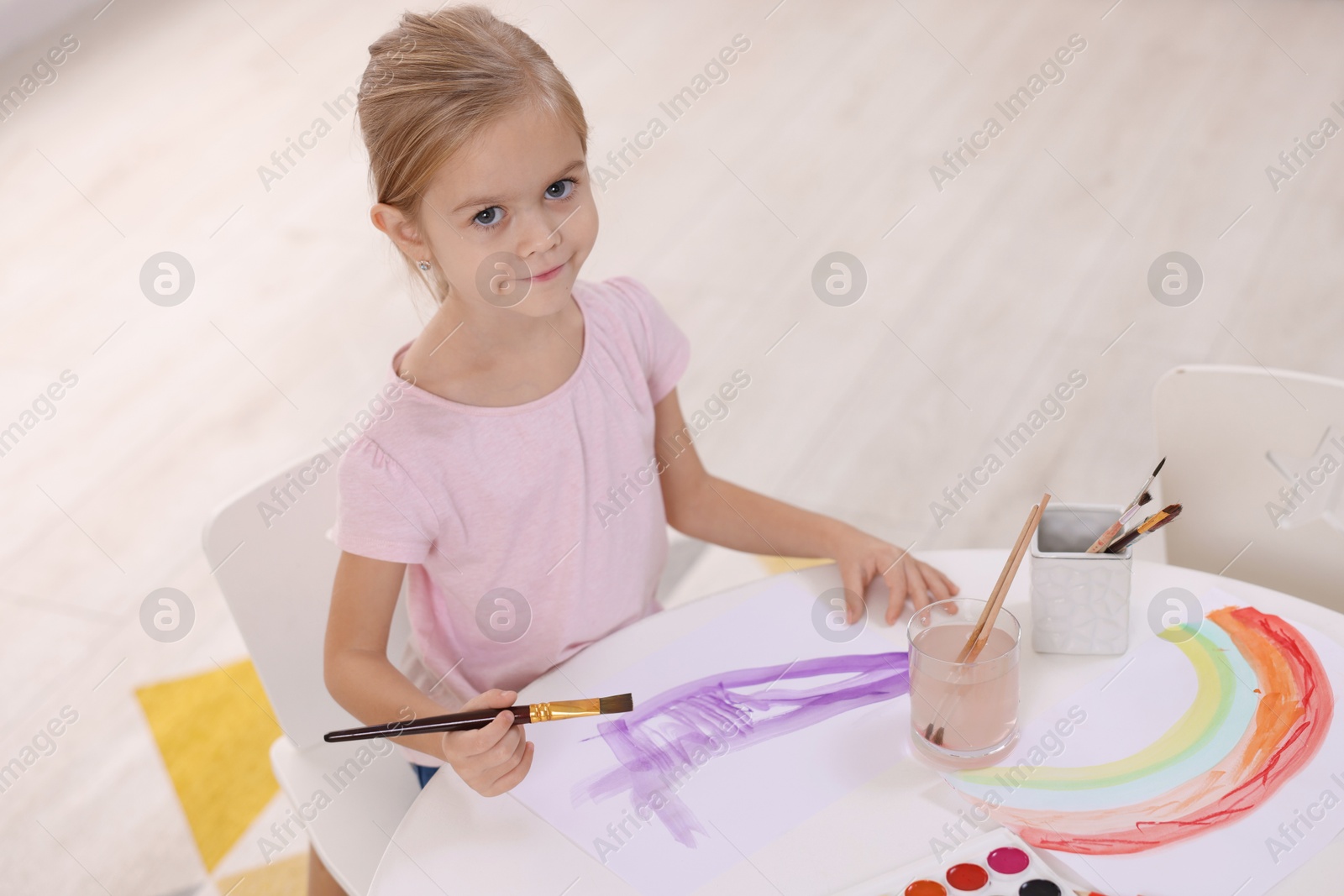 Photo of Cute girl drawing at white table indoors