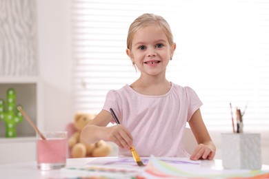 Photo of Smiling girl drawing at white table in kindergarten