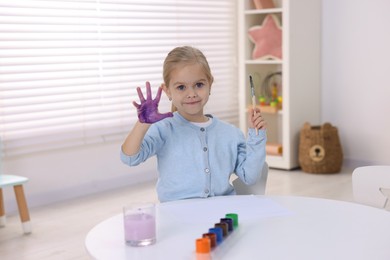 Photo of Cute girl drawing with palm at white table in kindergarten