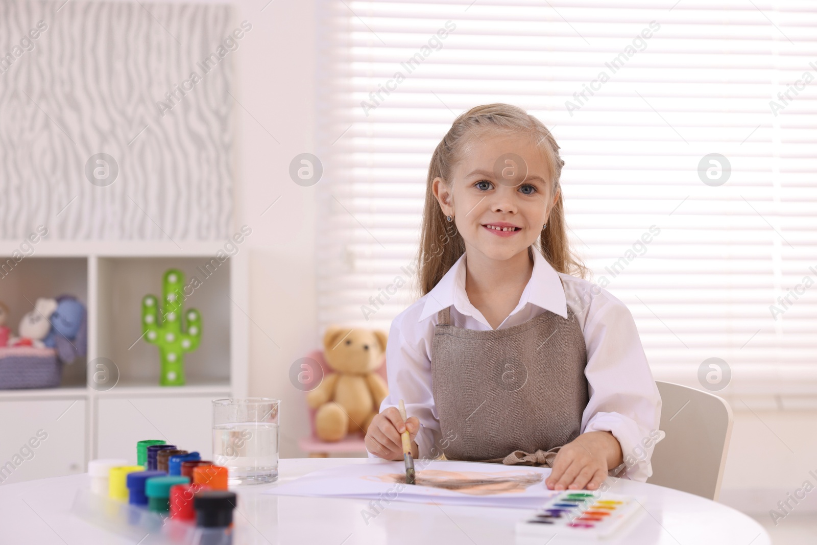 Photo of Smiling girl drawing at white table in kindergarten