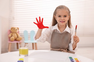 Photo of Happy girl drawing with palm at white table in kindergarten