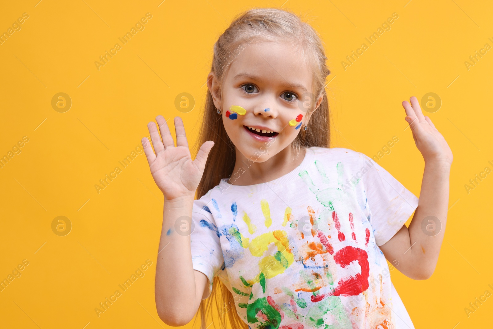 Photo of Portrait of smiling girl smeared in paint on orange background. Space for text