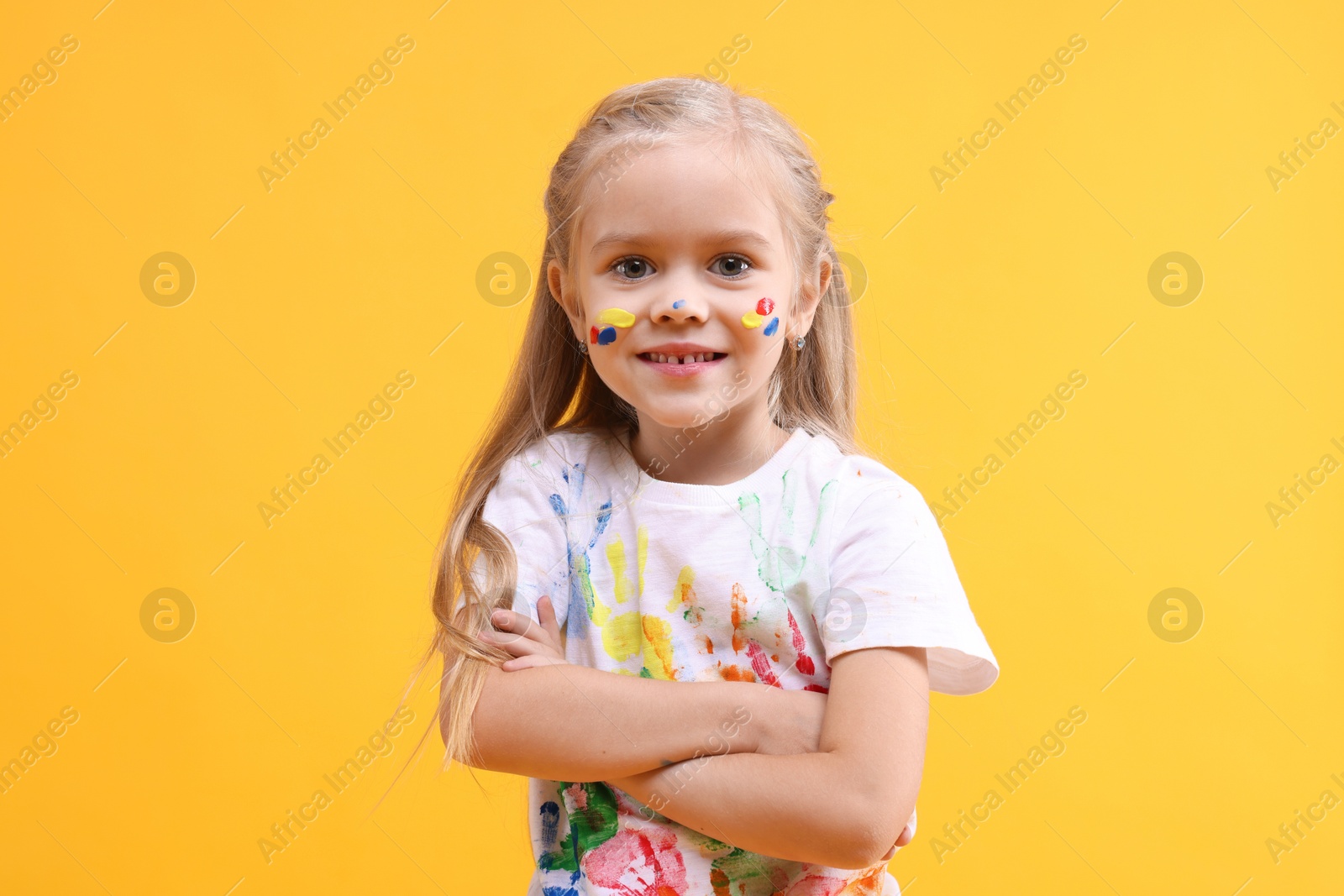 Photo of Smiling girl with crossed arms smeared in paint on orange background