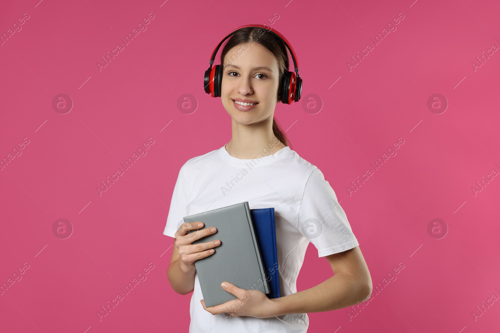 Photo of Portrait of smiling teenage girl in headphones with books on pink background