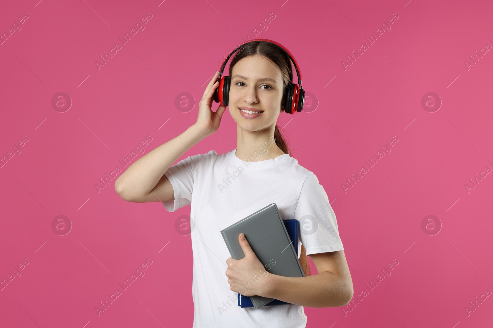 Photo of Portrait of smiling teenage girl in headphones with books on pink background