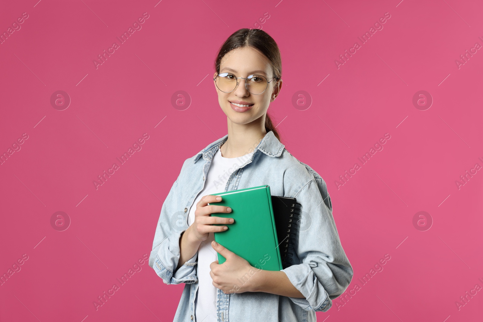 Photo of Portrait of smiling teenage girl with books on pink background