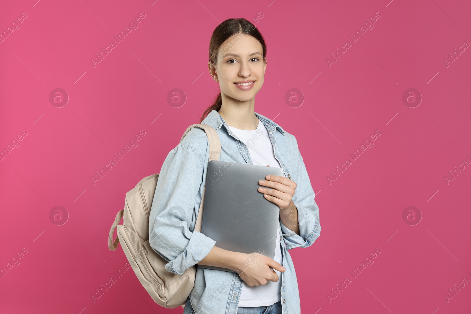 Photo of Portrait of smiling teenage girl with laptop on pink background