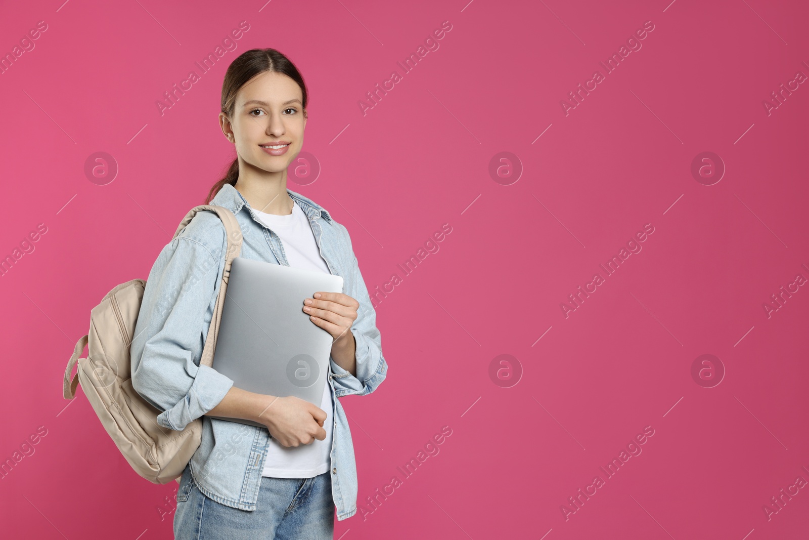 Photo of Portrait of smiling teenage girl with laptop on pink background. Space for text