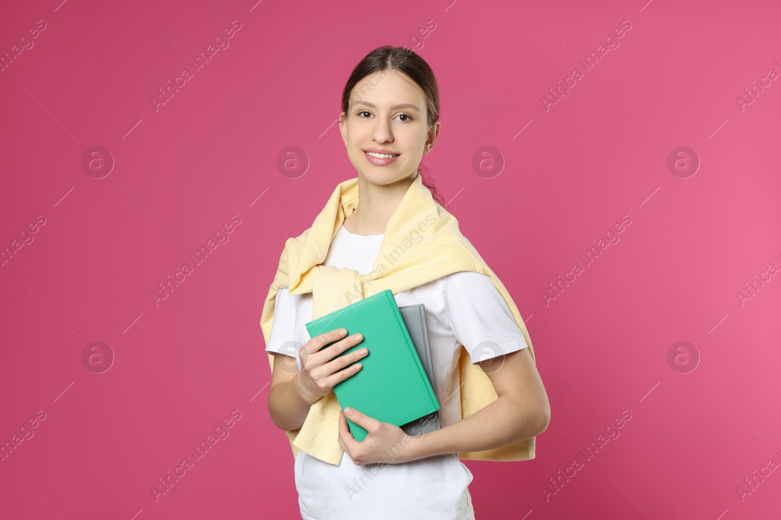 Photo of Portrait of smiling teenage girl with books on pink background