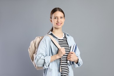 Photo of Portrait of smiling teenage girl with books and backpack on grey background