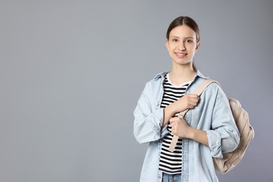 Photo of Portrait of smiling teenage girl in headphones with backpack on grey background. Space for text