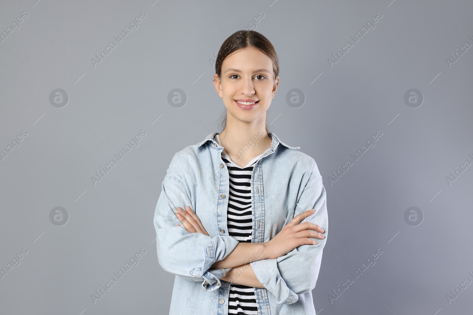 Photo of Portrait of smiling teenage girl with crossed arms on grey background