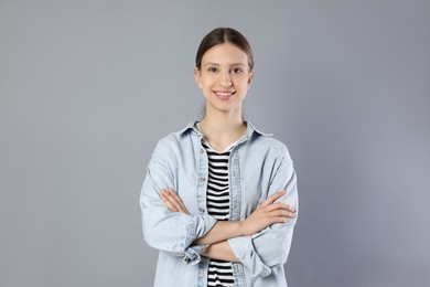 Photo of Portrait of smiling teenage girl with crossed arms on grey background