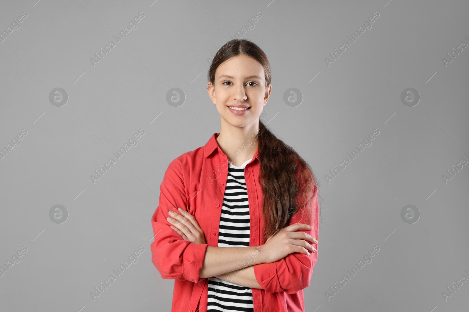 Photo of Portrait of smiling teenage girl with crossed arms on grey background