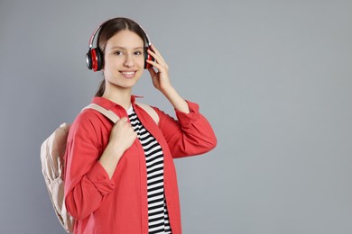 Photo of Portrait of smiling teenage girl in headphones with backpack on grey background. Space for text