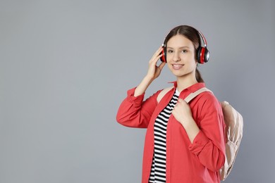 Photo of Portrait of smiling teenage girl in headphones with backpack on grey background. Space for text