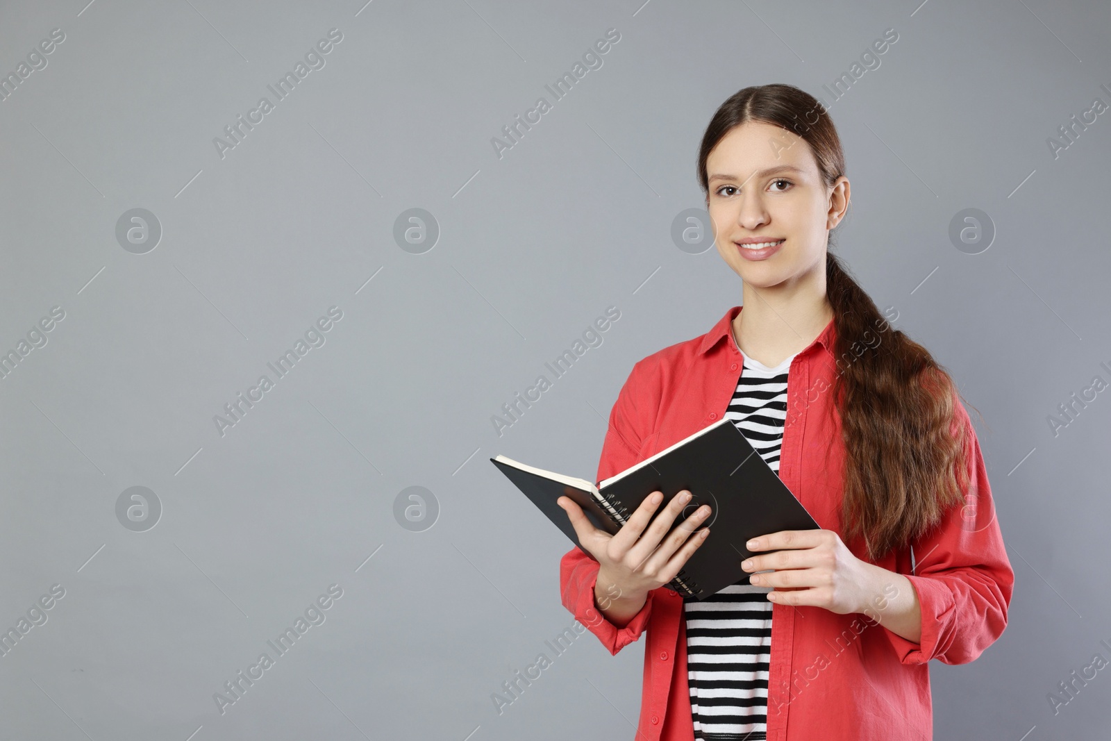 Photo of Portrait of smiling teenage girl with book on grey background. Space for text