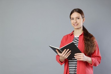 Photo of Portrait of smiling teenage girl with book on grey background. Space for text