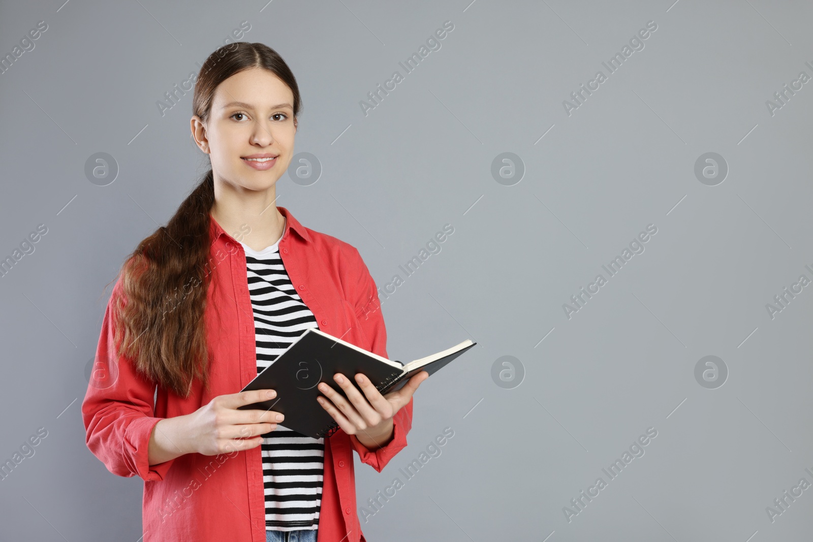 Photo of Portrait of smiling teenage girl with book on grey background. Space for text