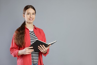 Photo of Portrait of smiling teenage girl with book on grey background. Space for text