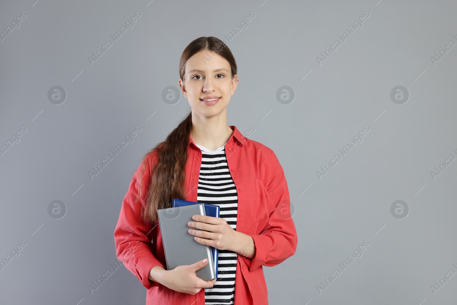 Photo of Portrait of smiling teenage girl with books on grey background