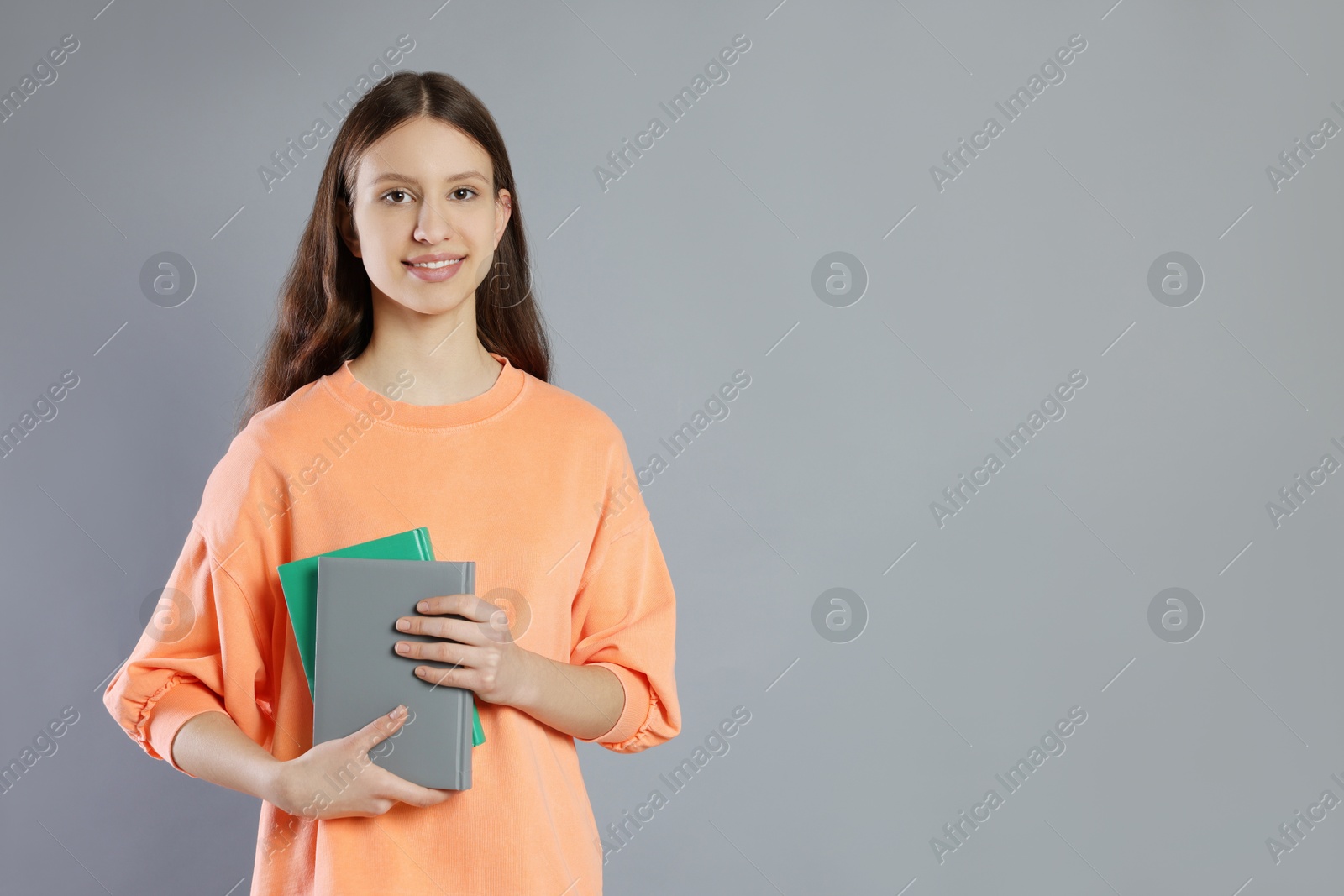 Photo of Portrait of smiling teenage girl with books on grey background. Space for text