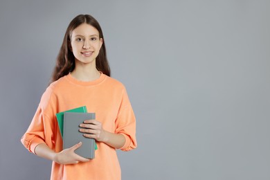 Photo of Portrait of smiling teenage girl with books on grey background. Space for text