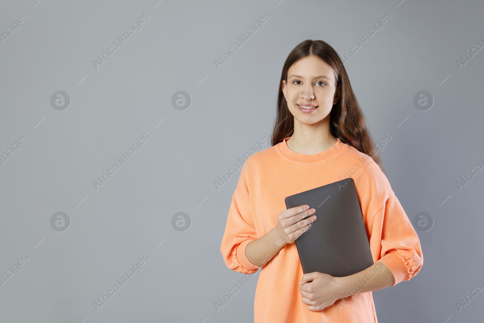 Photo of Portrait of smiling teenage girl with laptop on grey background. Space for text