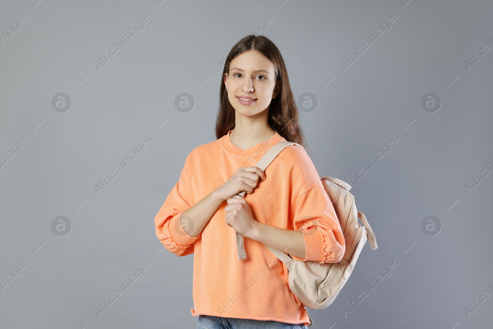 Photo of Portrait of smiling teenage girl with backpack on grey background