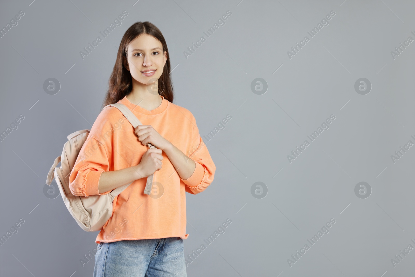 Photo of Portrait of smiling teenage girl with backpack on grey background. Space for text